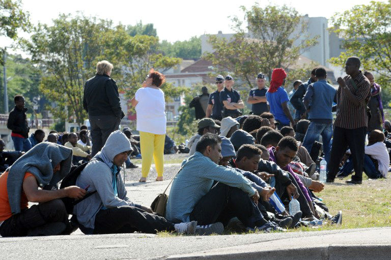 Observados por policiais franceses, imigrantes aguardam a distribuição de comida por uma ONG local em Calais, porto na França usado para entrar no Reino Unido 
