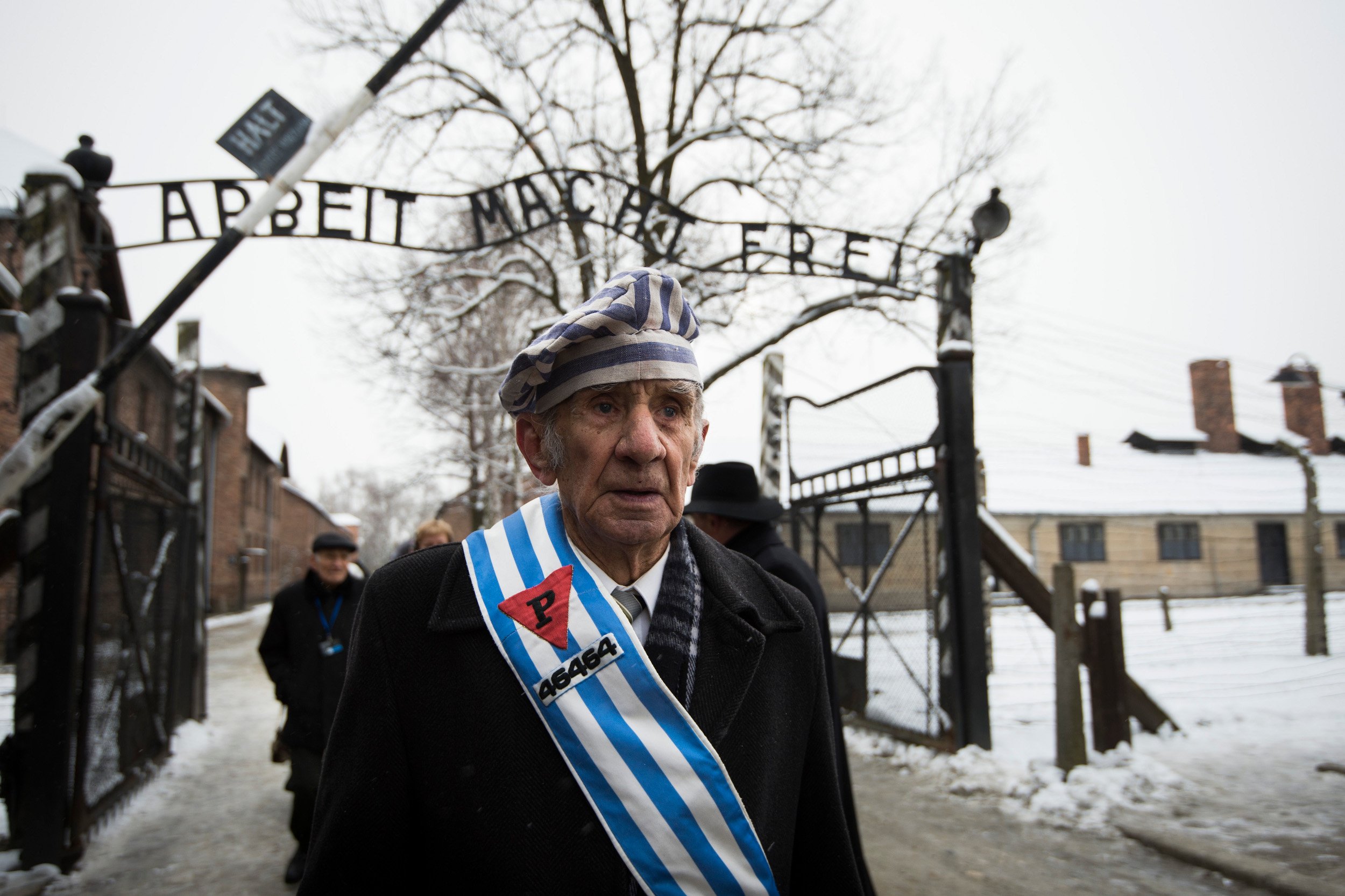 O sobrevivente de Auschwitz, Miroslaw Celka, caminha pelo portão do antigo campo de concentração que tem os dizeres 