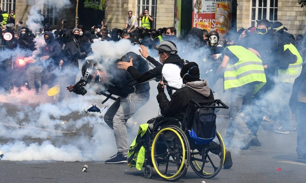 FRANÇA: Cinegrafista reage após ser atingido por uma bomba de gás lacrimogêneo enquanto um manifestante vai ajudá-lo durante confrontos com a polícia (Foto: Alain Jocard/AFP)