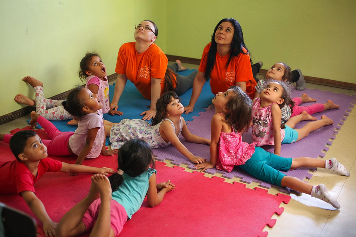 Alunos na aula de yoga|Ioga ajuda a promover educação|Criança recebendo massagem Shantala|Yoga para crianças|Shantala para crianças|Yoga para crianças|Yoga para crianças