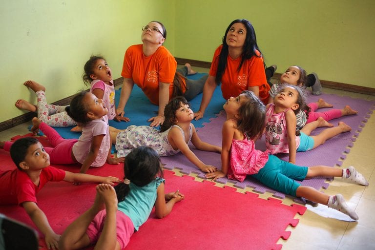 Alunos na aula de yoga|Ioga ajuda a promover educação|Criança recebendo massagem Shantala|Yoga para crianças|Shantala para crianças|Yoga para crianças|Yoga para crianças