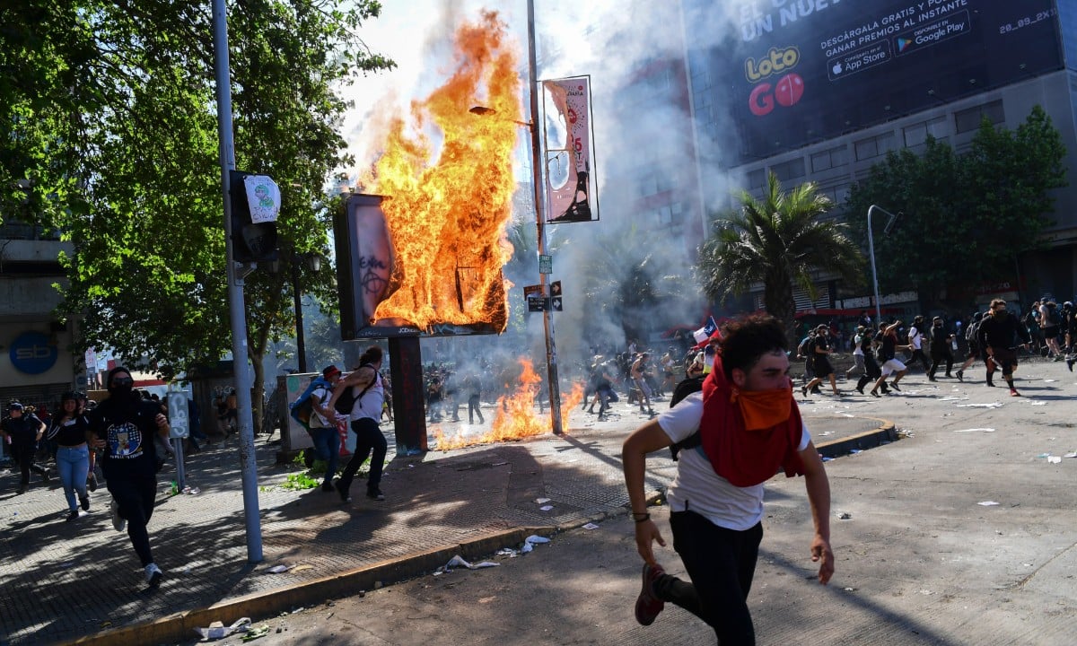 Manifestante corre em meio ao cenário de caos que tomou o Chile durante atos contra o aumento do preço (Foto: Martin  Bernetti/AFP) 