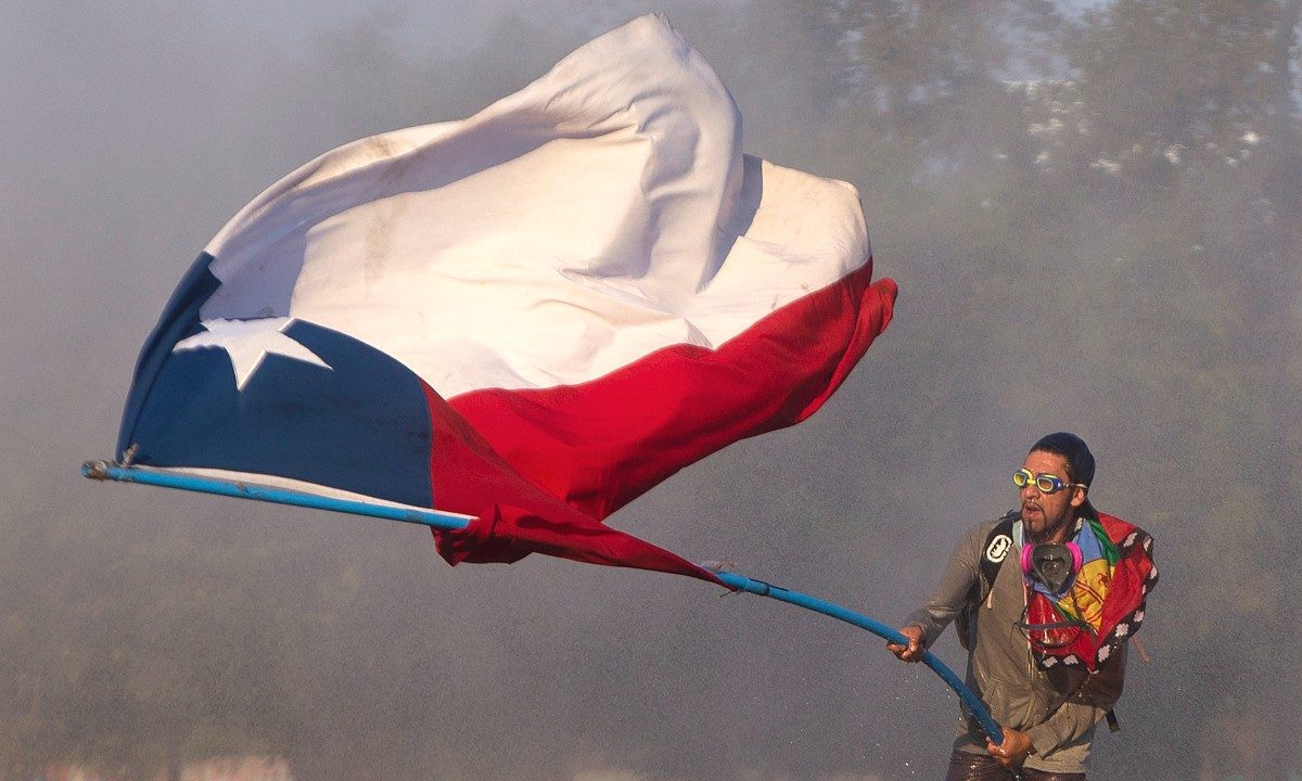 Jovem chileno balança enorme bandeira do Chile durante protestos na capital Santiago - Foto: Claudio Reyes/AFP