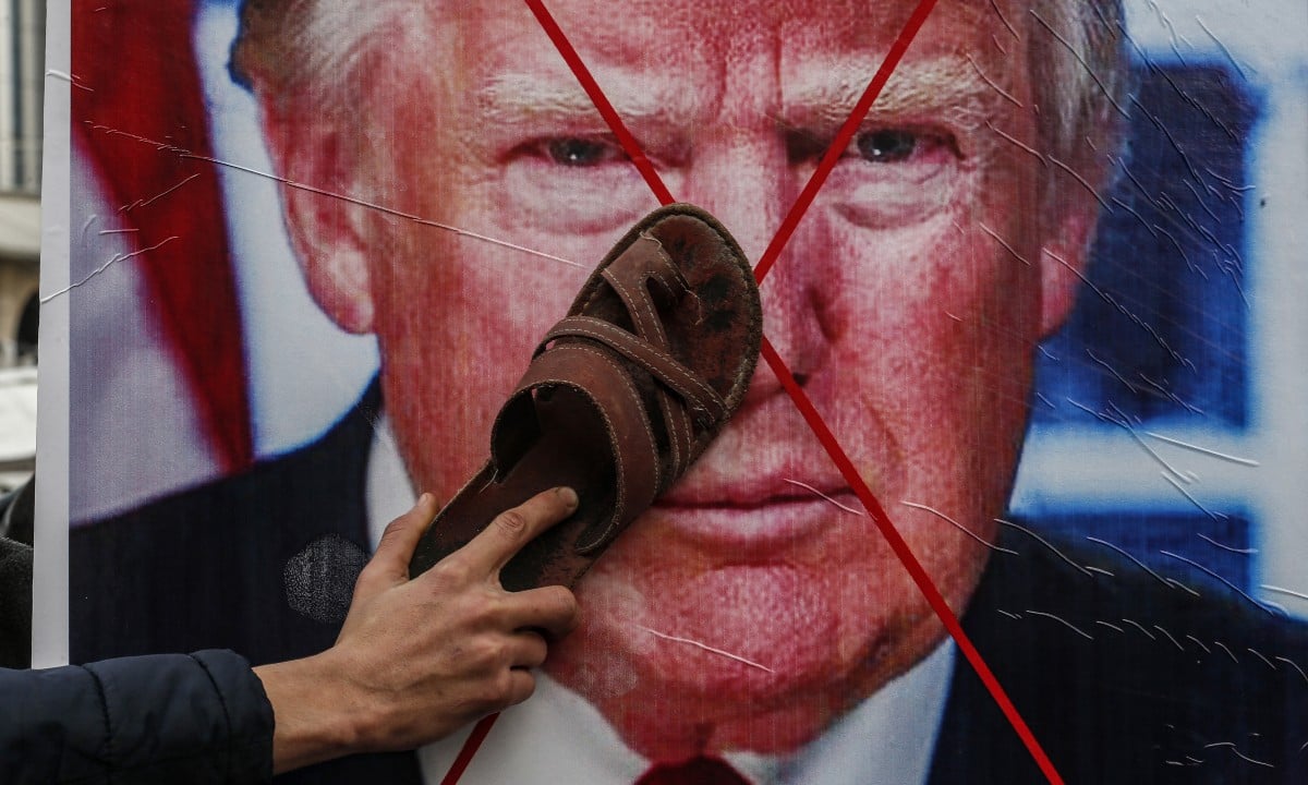 Manifestante bate com um chinelo em foto do presidente americano Donald Trump (Foto SAID KHATIB / AFP) 