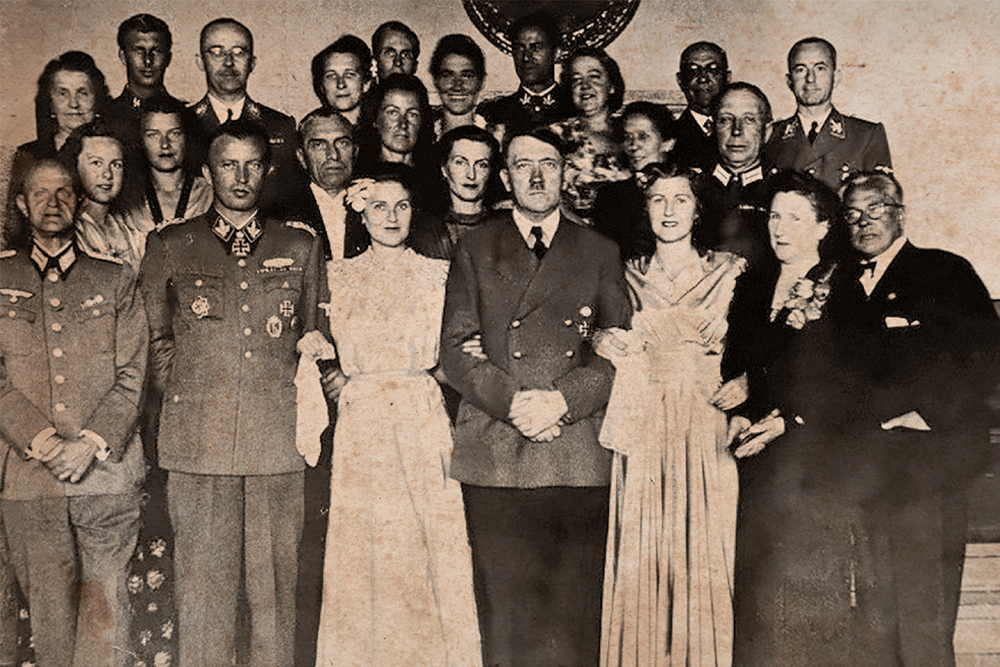 Fegelein e Gretl Braun na festa de casamento, com Hitler e Eva. Himmler está ao fundo na mesma direção de Fegelein; e o seu irmão Waldemar é o primeiro à esq. na última fileira - Imagem: Alamy/Fotoarena e Arquivo Público da Alemanha 