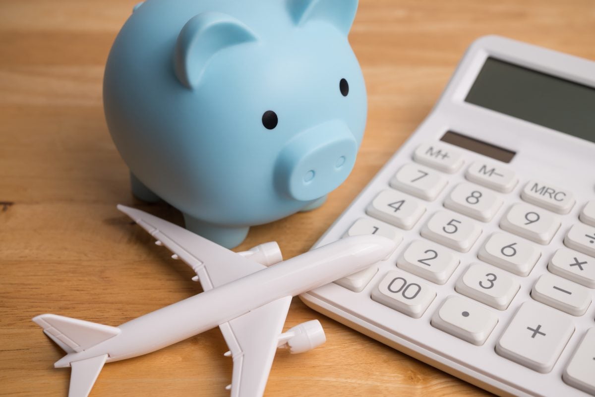 Blue piggy bank, airplane and white calculator on wooden table background. Travel budget, buying flight ticket and hotel booking, savings and money management for travel holiday, home finance concept. 