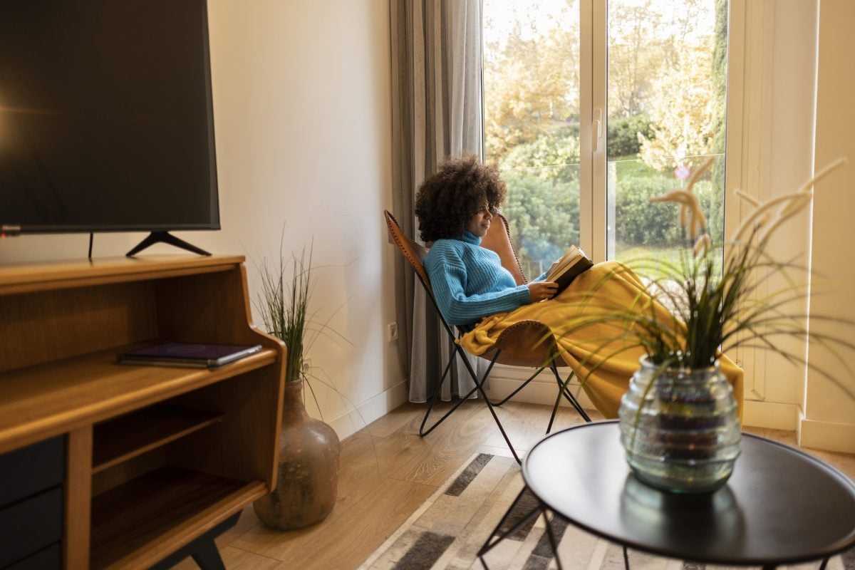pretty african american woman reading a book in the living room at home 